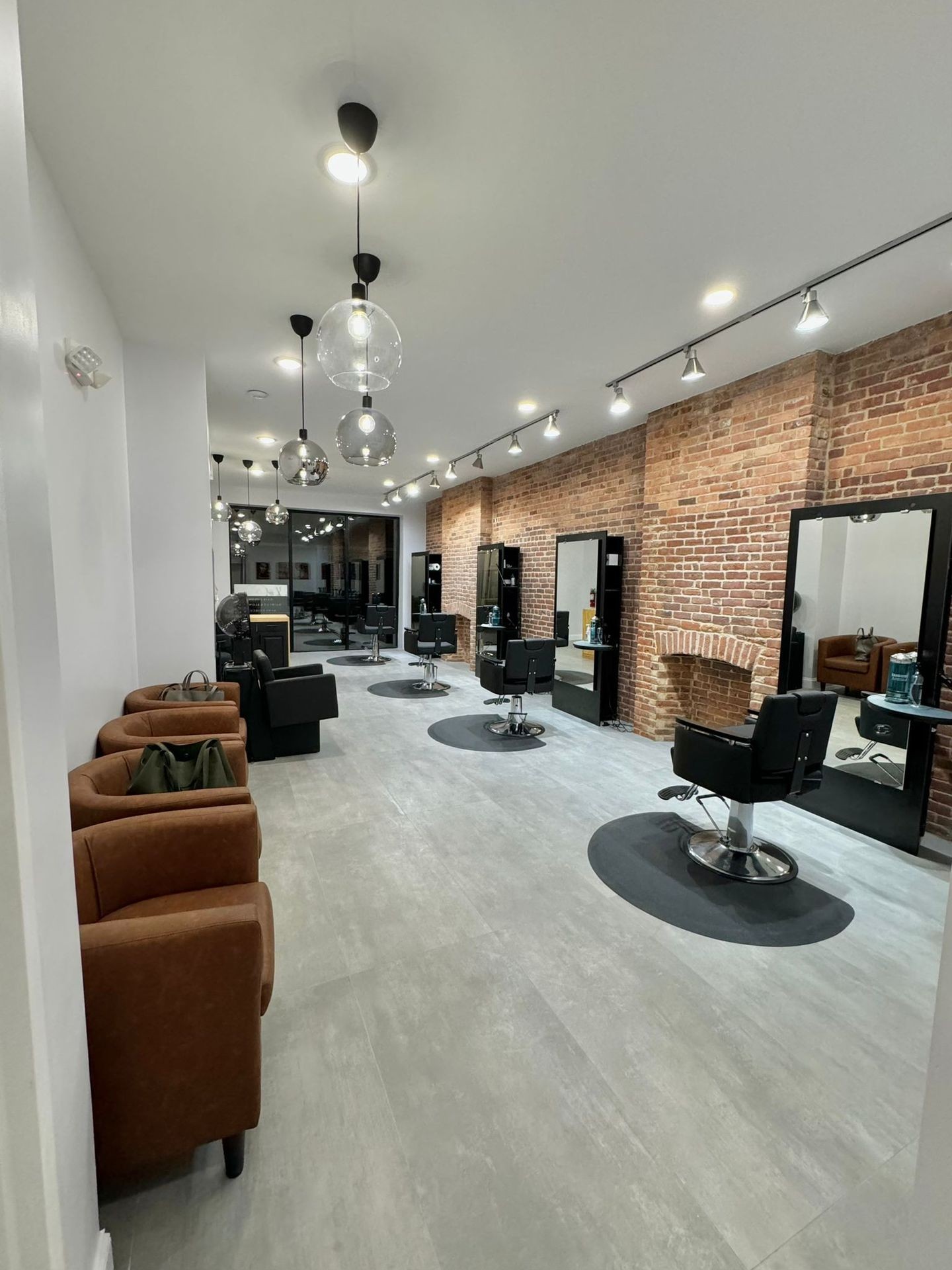 Modern hair salon with brick walls, leather chairs, mirrors, and hanging pendant lights.