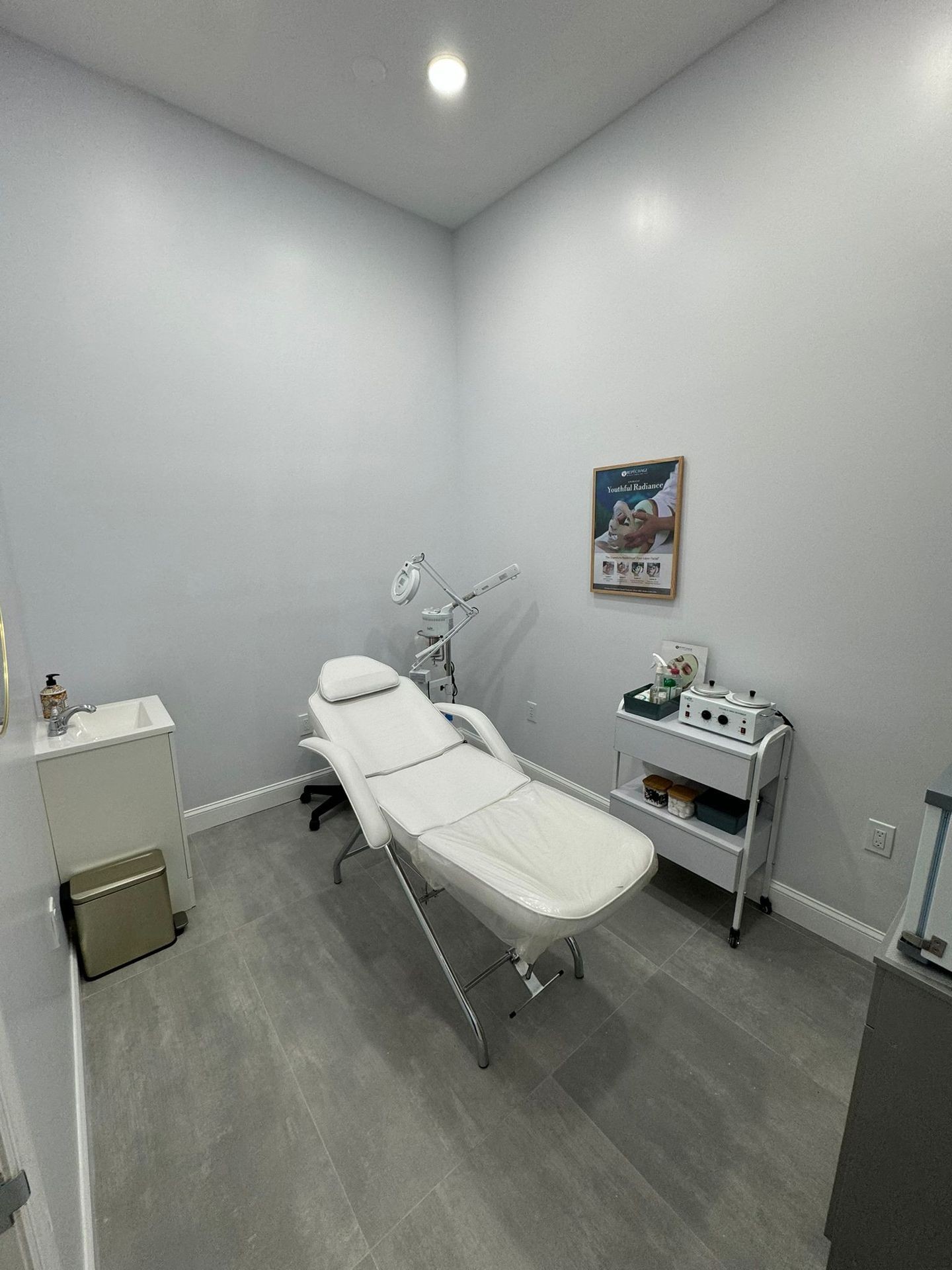 Minimalist spa room with a massage table, side cart, and sink.